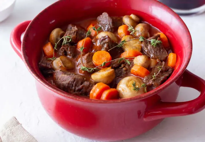 Un plat rouge rempli de bœuf bourguignon facile, avec des morceaux de bœuf tendres, des carottes et des champignons, garni de thym frais.