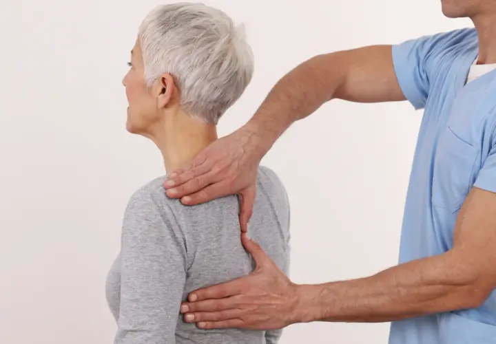 Fizjoterapeuta masuje górną część pleców i łopatki kobiety.