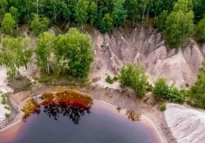 Widok z lotu ptaka na krajobraz przypominający łuk mużakowa z kosmosu, z wodą i drzewami.