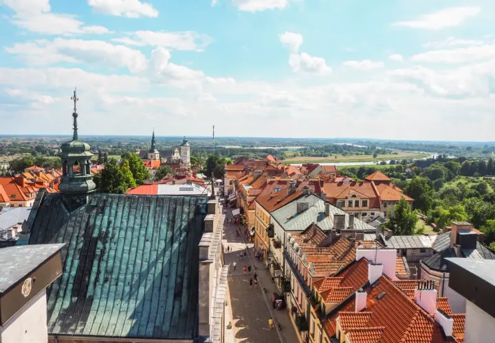 Widok z góry na urokliwy sandomierz rynek z brukowaną uliczką, kamieniczkami i kościelnymi wieżami w tle.