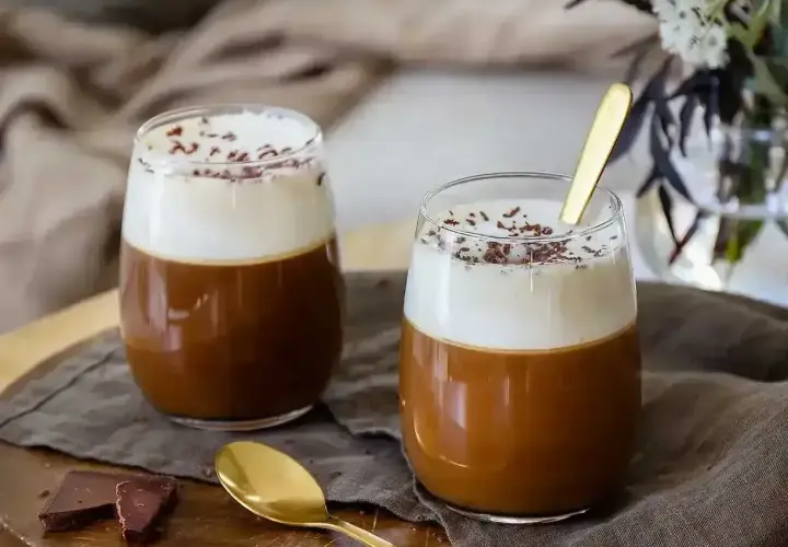 Två glas med krämig irish coffee, toppad med vispgrädde och chokladströssel. En gyllene sked vilar i det ena glaset.