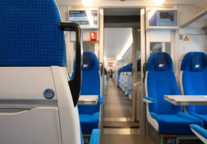 Wnętrze pociągu PKP Intercity. Siedzenia w kolorze niebieskim, rzędy foteli po obu stronach korytarza.