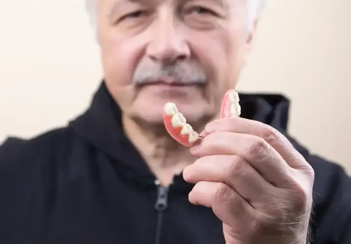 Starszy mężczyzna trzyma protezę. Dowiedz się, jak usunąć klej do protez z dziąseł, aby zapewnić komfort.