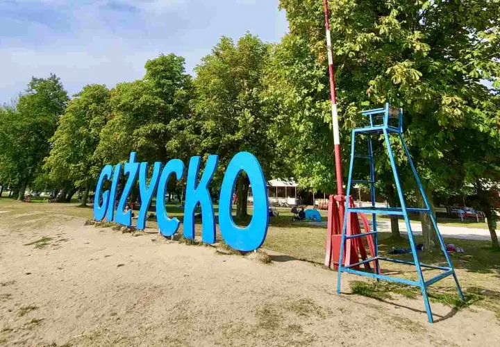Napis GIŻYCKO na plaży, obok ratownicza wieża. Idealne miejsce na wakacje, mnóstwo giżycko atrakcje dla dzieci.