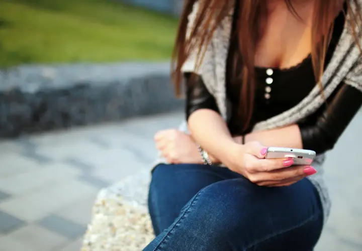 Dziewczyna z różowym lakierem na paznokciach pisze sms-a, zastanawiając się, jak wkręcić chłopaka przez sms.