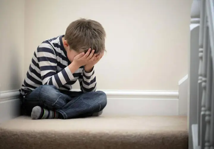 Bambino seduto sulle scale, con le mani sul viso, simbolo della delusione dei figli.