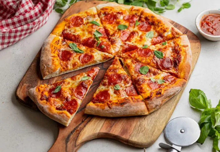 Apetyczna pizza pepperoni z ciągnącym się serem i świeżą bazylią, podana na drewnianej desce.