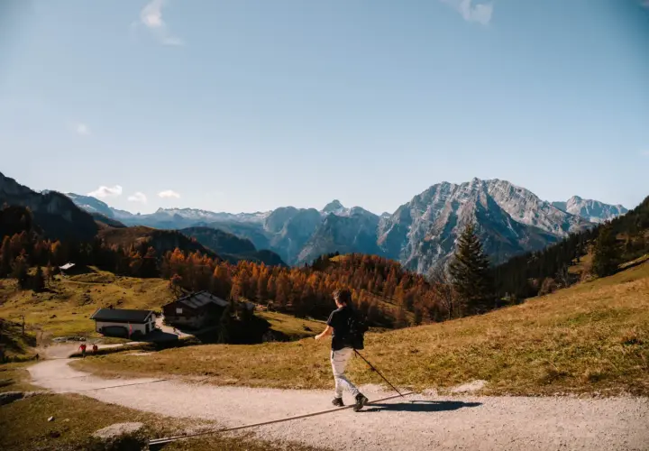 A lone hiker enjoys a scenic autumn day hiking in Bavaria, with colorful trees and majestic mountains in the background.