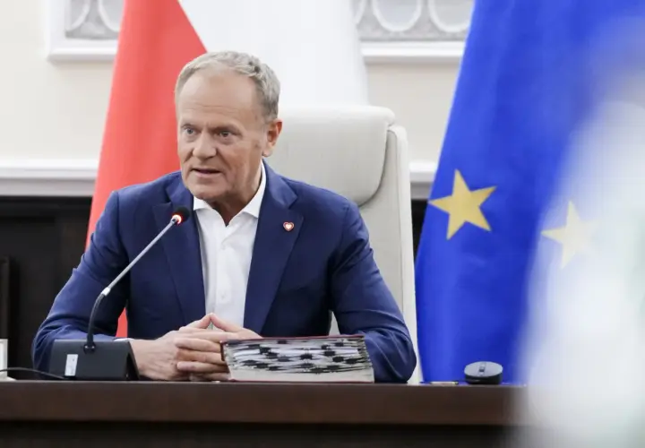 Donald Tusk w Sosnowcu, przemawia przy mikrofonie, za nim flagi Polski i UE.