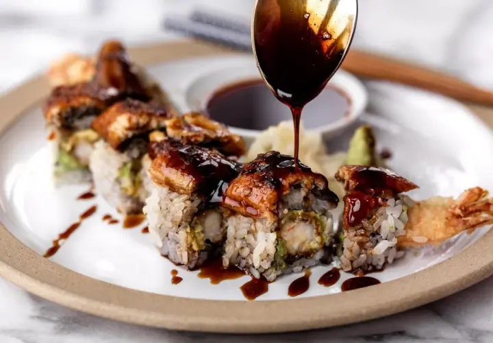 A spoon drizzles rich unagi sauce over a delicious sushi roll, showcasing how to make unagi sauce for a perfect finish.