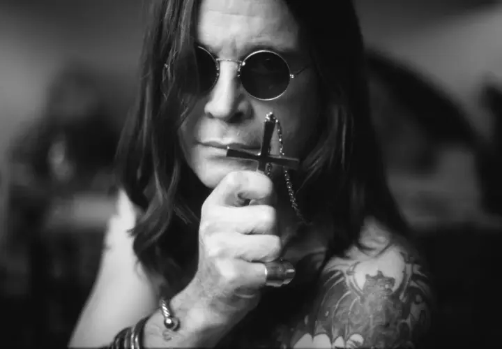 Ozzy Osbourne, ikona zespołu Black Sabbath, w okularach i z krzyżem w dłoni.