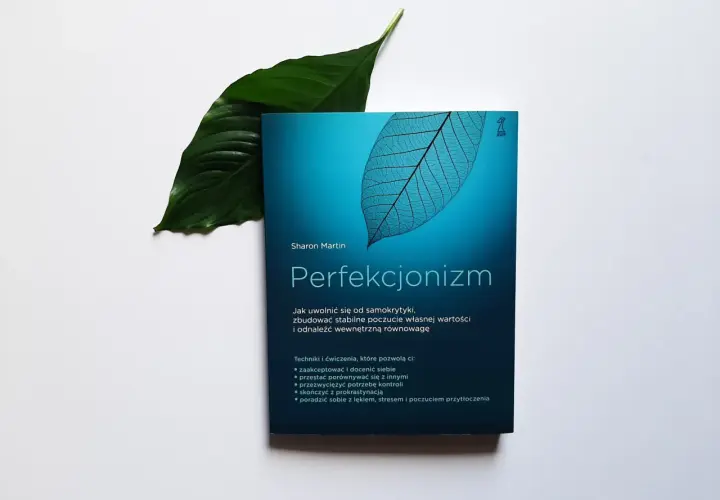 Książka "Perfekcjonizm" Sharon Martin, z liściem w tle, obiecuje uwolnienie od samokrytyki i budowanie wewnętrznej równowagi.