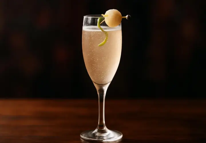 Ett elegant drink med bubbel, garnerat med en citronskalsslinga och en rund fruktbit på en cocktailpinne.