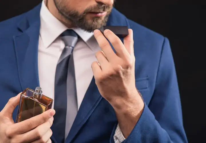Mężczyzna w garniturze wącha perfumy z buteleczki.