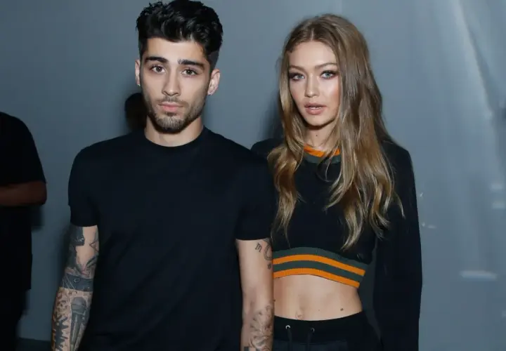 Zayn Malik i Gigi Hadid pozują razem, oboje ubrani na czarno. Zayn ma tatuaże na ramionach, a Gigi odsłania brzuch w krótkim topie.