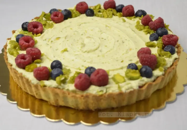 Tarta pistacjowa z białą czekoladą, ozdobiona malinami, borówkami i pistacjami.