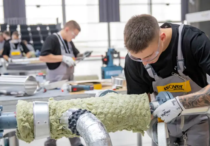 Młody mężczyzna w okularach ochronnych i fartuchu pracuje nad izolacją rury. Dbałość o detale i precyzja zapewniają dobrą adhezję materiału izolacyjnego.