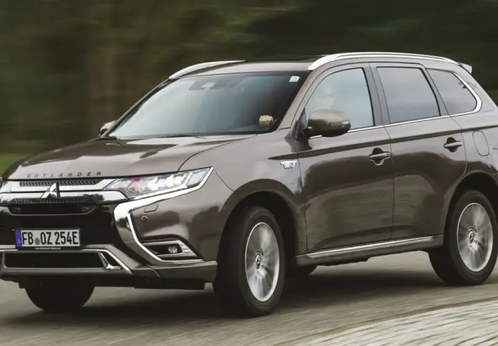 Brązowy Mitsubishi Outlander PHEV jedzie po drodze, z rozmytym tłem lasu.