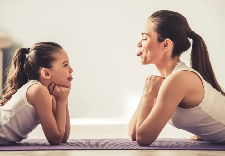 Mama i córka ćwiczą, wyciągając języki. Widać zaangażowanie mięśni wewnętrznych języka w zabawną zabawę.