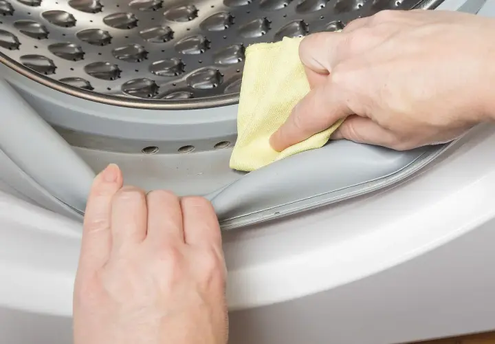 Manos limpian la goma de la lavadora con un paño amarillo para saber como quitar el mal olor de la lavadora.