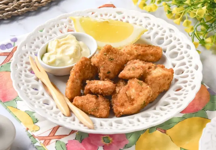 Deliciosas lagrimitas de pollo crujientes, servidas con mayonesa y limón en un plato blanco.