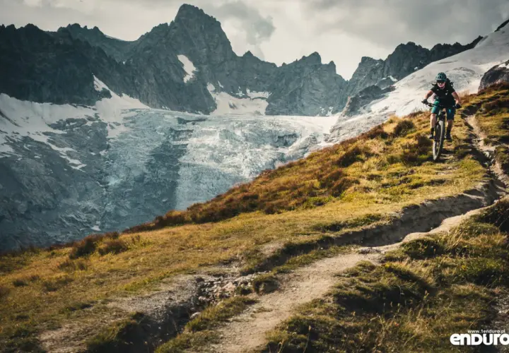 Rowerzysta na szlaku podczas Tour du Mont Blanc, z lodowcem i skalistymi szczytami w tle.