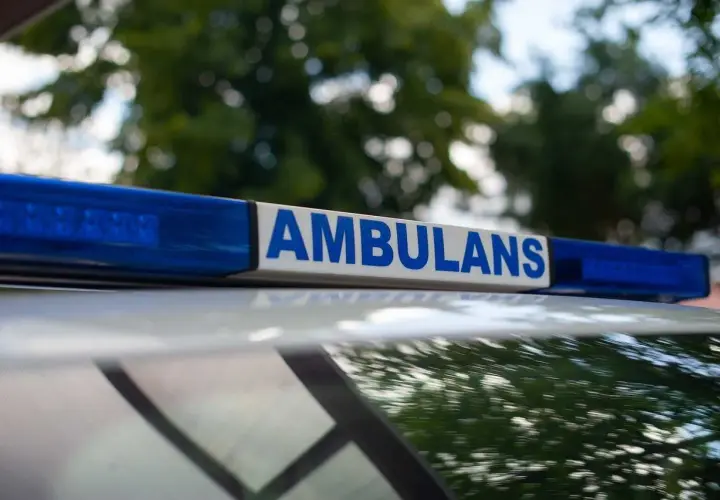 Napis "AMBULANS" na niebieskim świetle. Służby przyjechały na miejsce, gdzie doszło do zgonu w domu. Policja zabezpiecza teren.