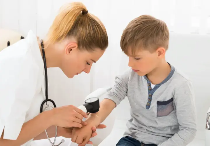 Lekarka bada rękę chłopca dermatoskopem, sprawdzając znamię dysplastyczne.