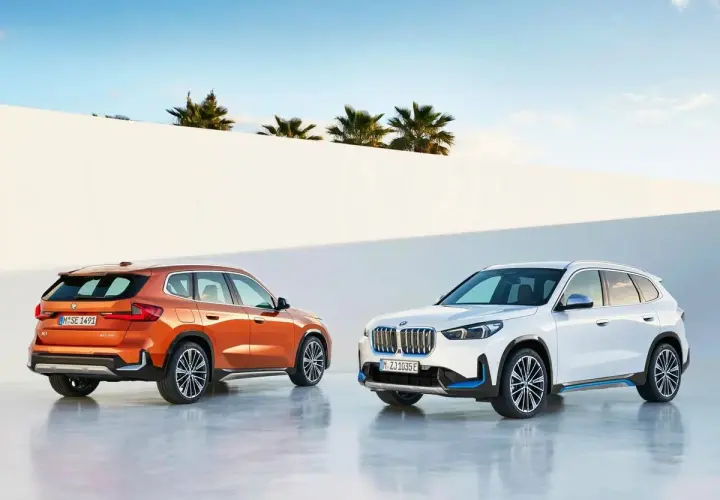 Dos BMW Serie X, uno naranja y otro blanco, posan ante un muro blanco y palmeras.