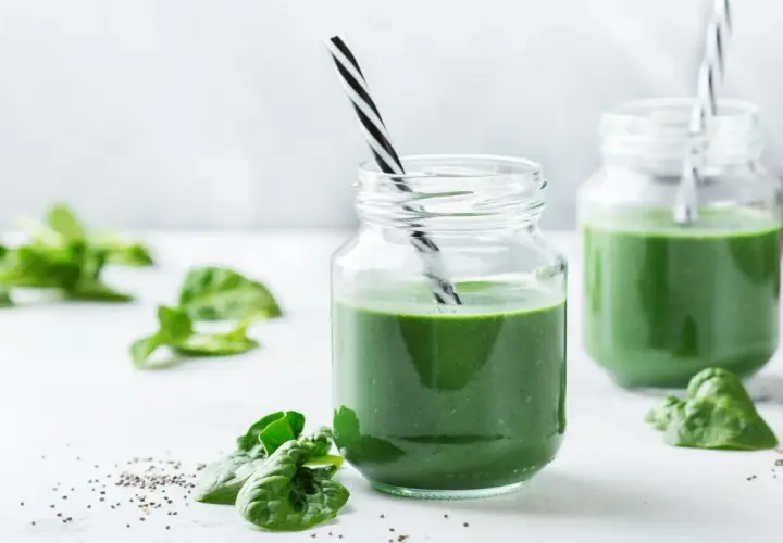 Två glas med grön smoothie, garnerade med spenatblad och chiafrön. Tänk på eventuella spirulina biverkningar innan du dricker.