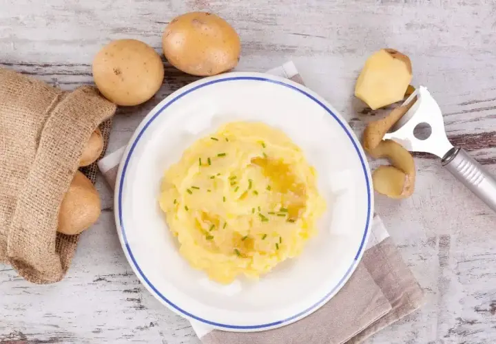 Pyszne puree ziemniaczane na talerzu, obok surowe ziemniaki i obieraczka. Czy cukrzyk może jeść ziemniaki? Tak, w umiarkowanych ilościach!