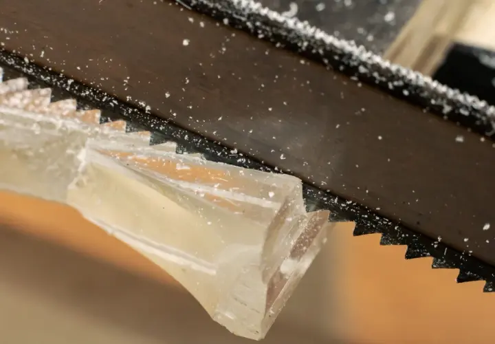 Sågtänder skär genom ett tjockt, genomskinligt material. Små bitar av kapa plexiglas flyger runt.