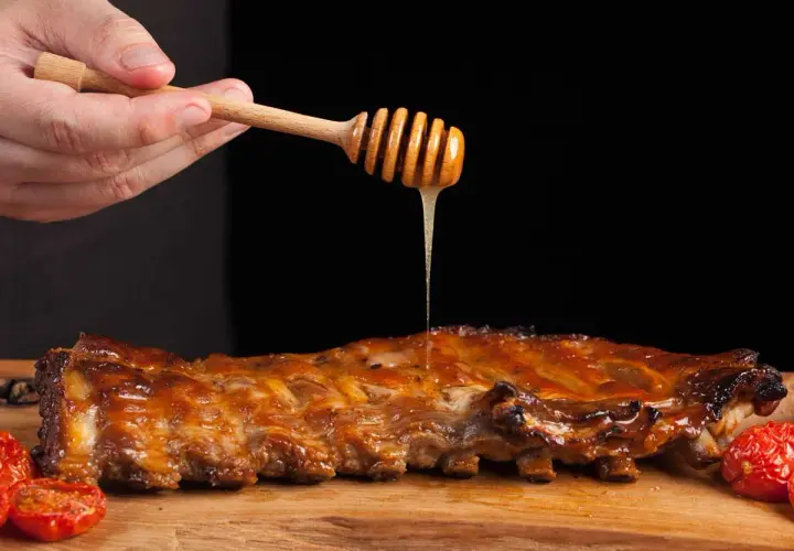 Costillas a la miel jugosas, bañadas con miel dorada de un palillo de madera. Acompañadas de tomates asados.