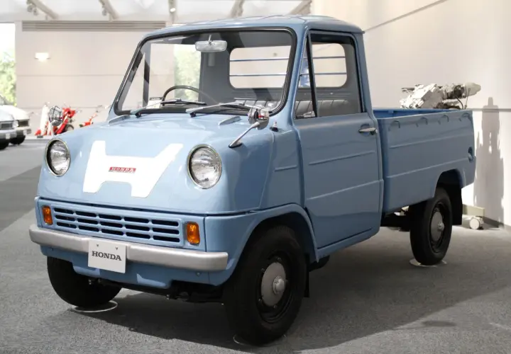 Niebieski, zabytkowy pick-up Honda z dużym białym "H" na masce. Ten model, choć nie jest Isuzu, przypomina klasyczne japońskie pojazdy użytkowe.