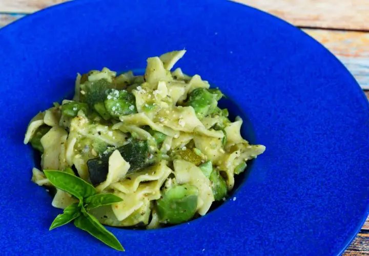 Pyszny makaron z bobem i cukinią, posypany parmezanem, podany na niebieskim talerzu.