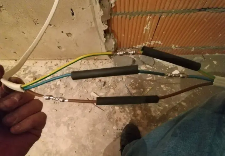 Ręczne skręcanie kabli elektrycznych, przygotowanie do izolacji. Widać połączenia przewodów w trakcie pracy.