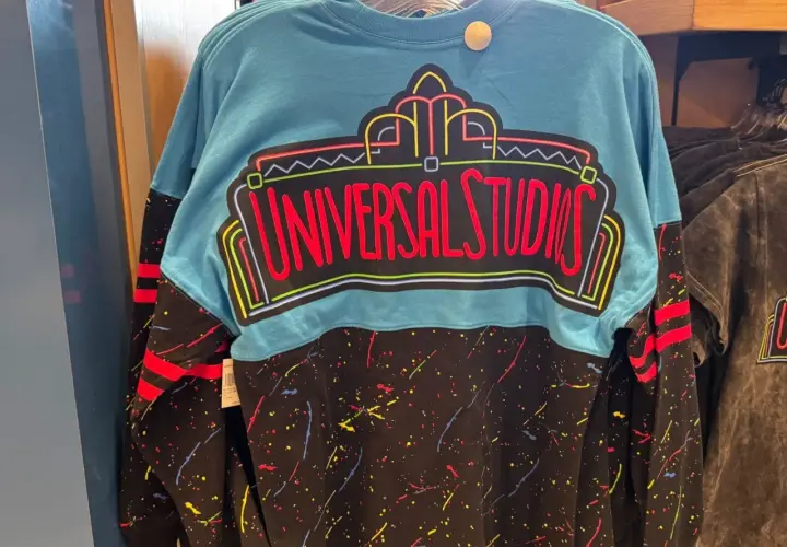 Turkusowy longsleeve z neonowym napisem "Universal Studios" i kolorowymi plamkami na czarnym tle. Idealny na wycieczkę do parku rozrywki!