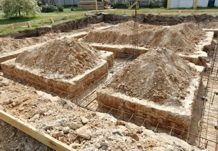 Wykop pod fundamenty bez szalunku, z widoczną zbrojeniem i usypaną ziemią.