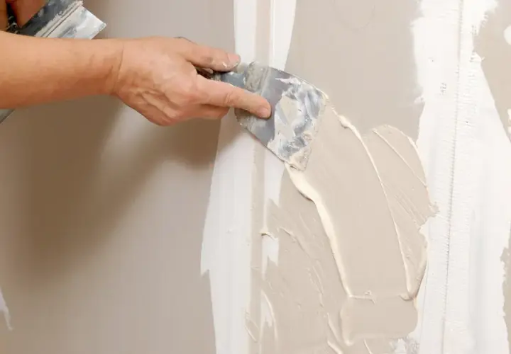 Mano stende stucco su una giuntura di cartongesso, ricordando che il cartongesso ha un verso.