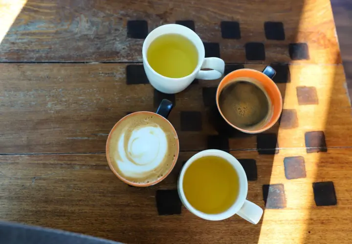 Kawa i herbata na drewnianym stole. Czy zielona herbata pobudza? Obok niej kawa latte i espresso.