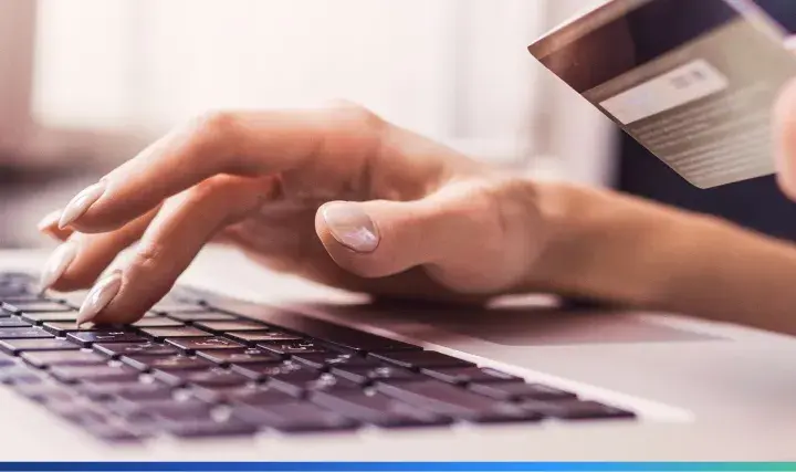 Dłonie wpisujące dane karty płatniczej na klawiaturze laptopa, ilustrujące najpopularniejsze metody płatności online.