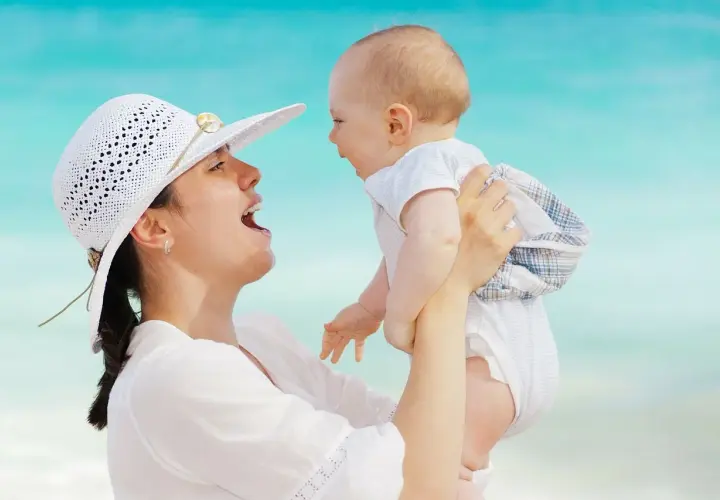 Mamma solleva il suo neonato di 5 mesi, forse le prime parole sono in arrivo, con il mare azzurro sullo sfondo.