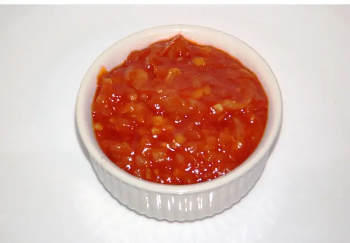Pomarańczowy, pikantny sos piri piri w białej miseczce, gotowy do podania.