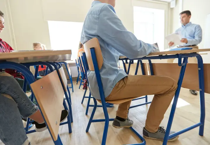 Uczniowie siedzą w ławkach, słuchając nauczyciela. Pomoc nauczyciela w szkole podstawowej to wsparcie w nauce i organizacji.