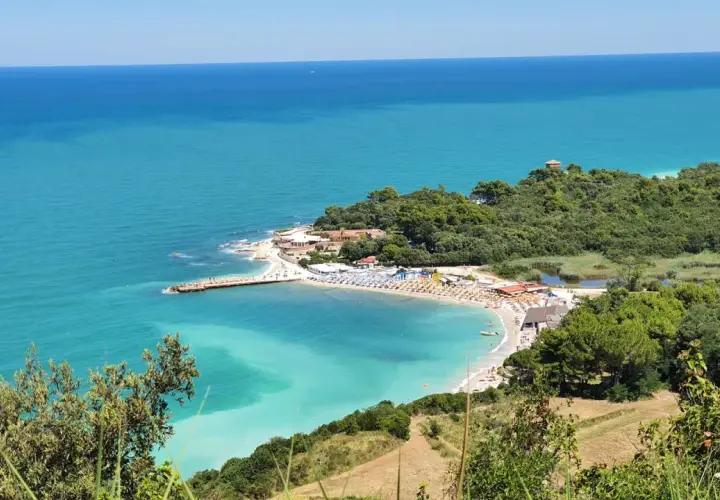 Vue panoramique de la baie de Portonovo, avec ses eaux turquoise, sa plage animée et sa végétation luxuriante.