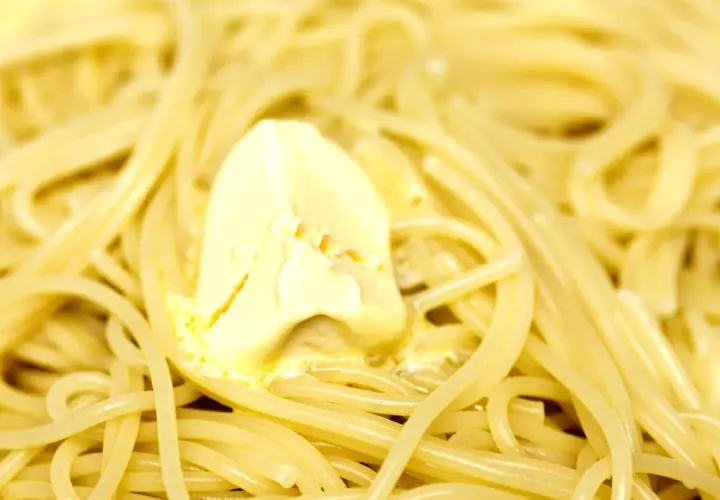 Un piatto di pasta in bianco, con spaghetti conditi da una generosa porzione di burro che si scioglie.