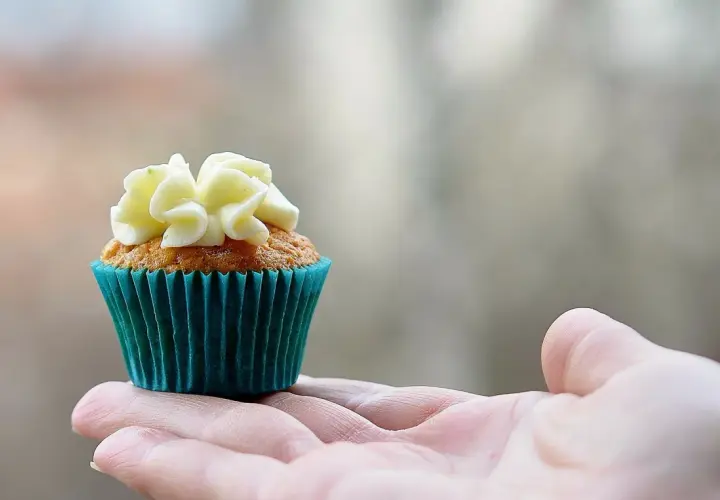 En hand håller en saftig muffins med vit frosting.