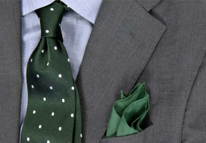 Elegancki zestaw: niebieska koszula, zielony krawat w kropki i szara marynarka w kratę. Idealna odpowiedź na pytanie: jaki krawat do niebieskiej koszuli.