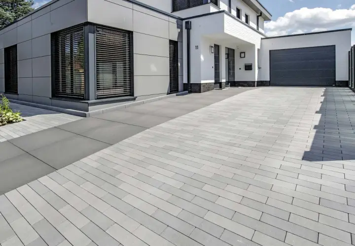 Moderne Einfahrt pflastern mit grauen Steinen. Das Haus hat eine graue Fassade und weiße Akzente.