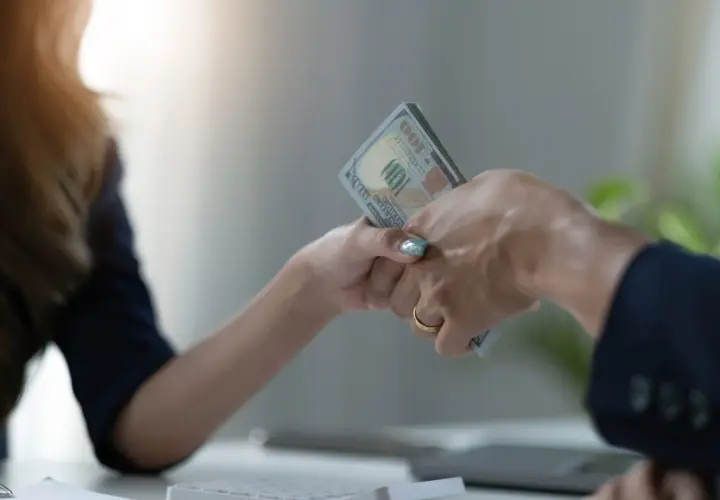 Dwie ręce przekazują sobie plik banknotów. To symboliczny moment zawarcia umowy pożyczki.